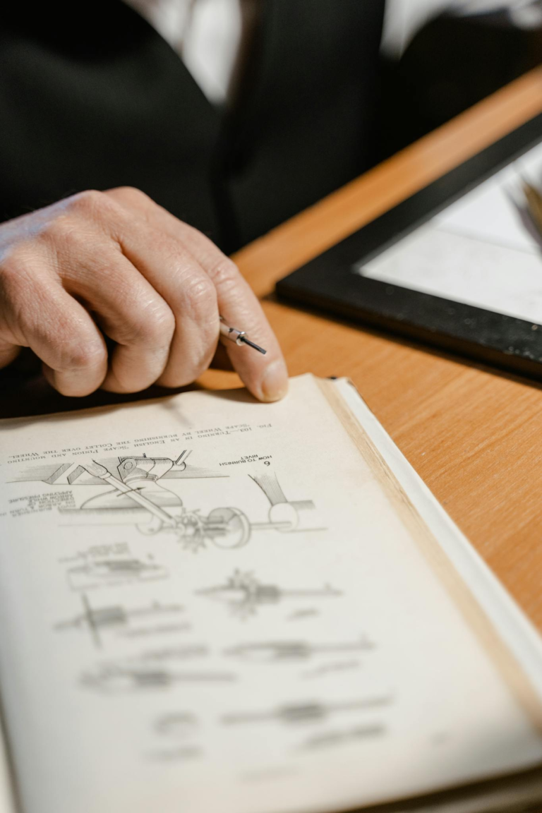 A hand holding a pen over an illustrative engineering book on a desk, emphasizing study focus.